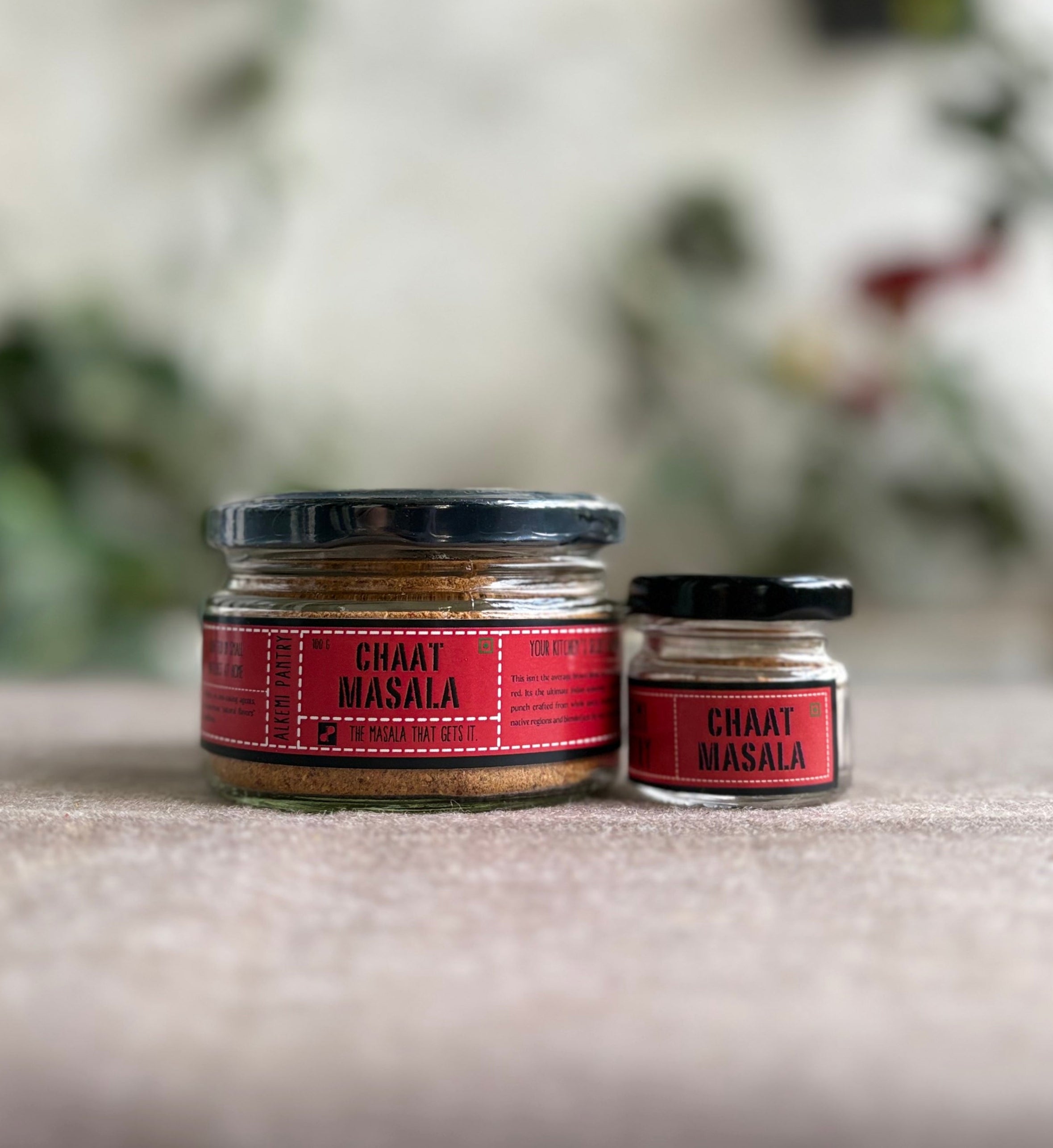 Two jars of 'Chaat Masala' on a surface with a blurred natural background