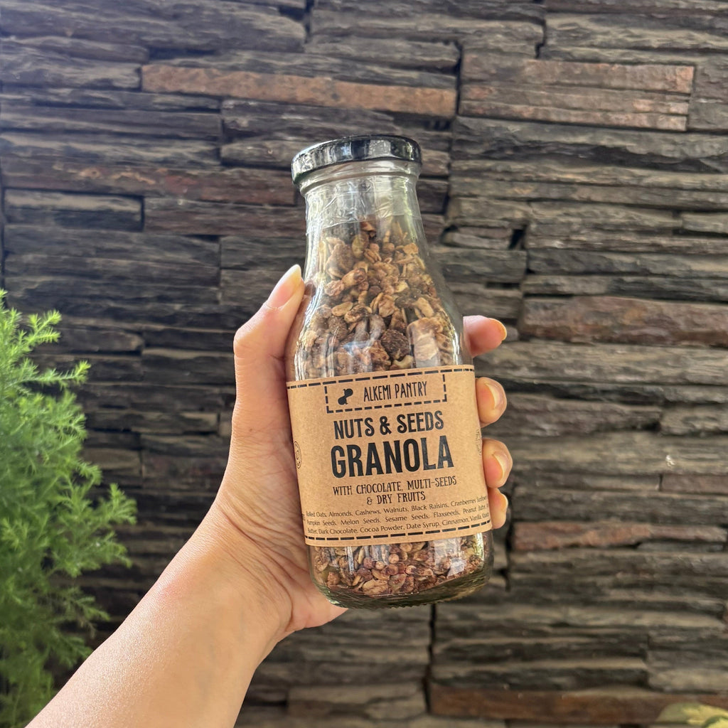 Hand holding a bottle of granola with a stone wall and plants in the background