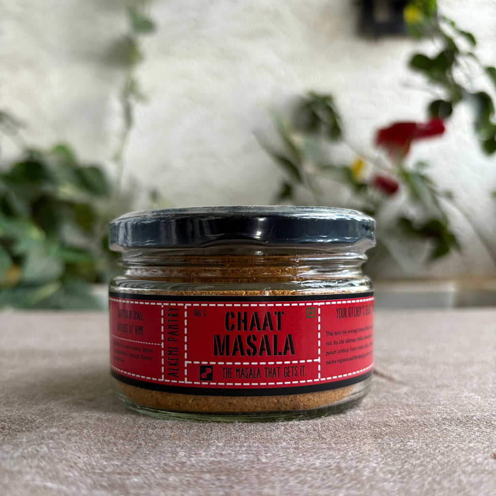 Jar of Chaat Masala against a neutral background with blurred greenery