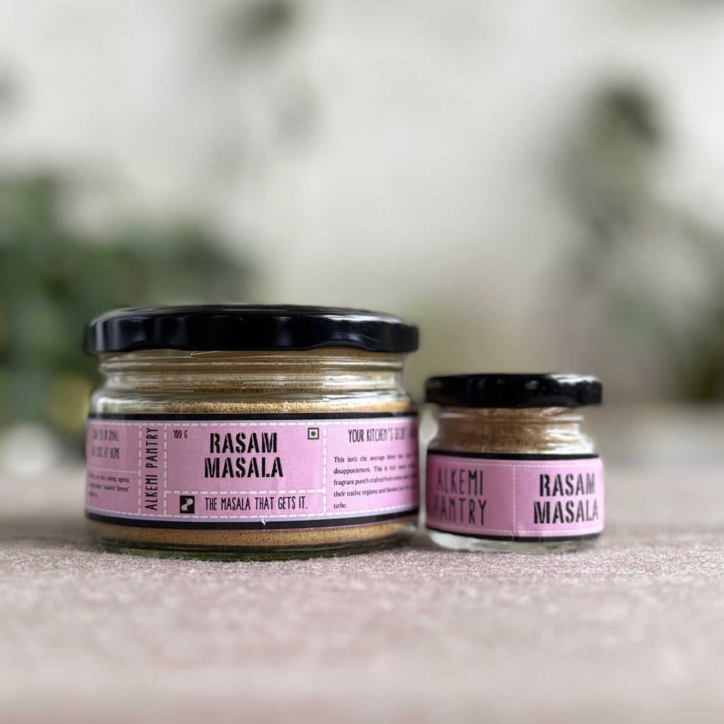 Two small jars of 'Rasam Masala' on a surface with a blurred natural background
